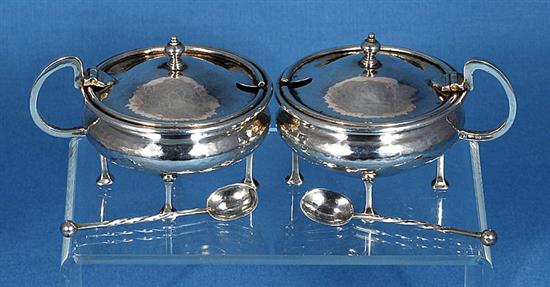 A pair of George V Arts & Crafts silver mustard pots with matching spoons, by Albert Edward Jones, width 90mm, weight 5.1oz/160grms.